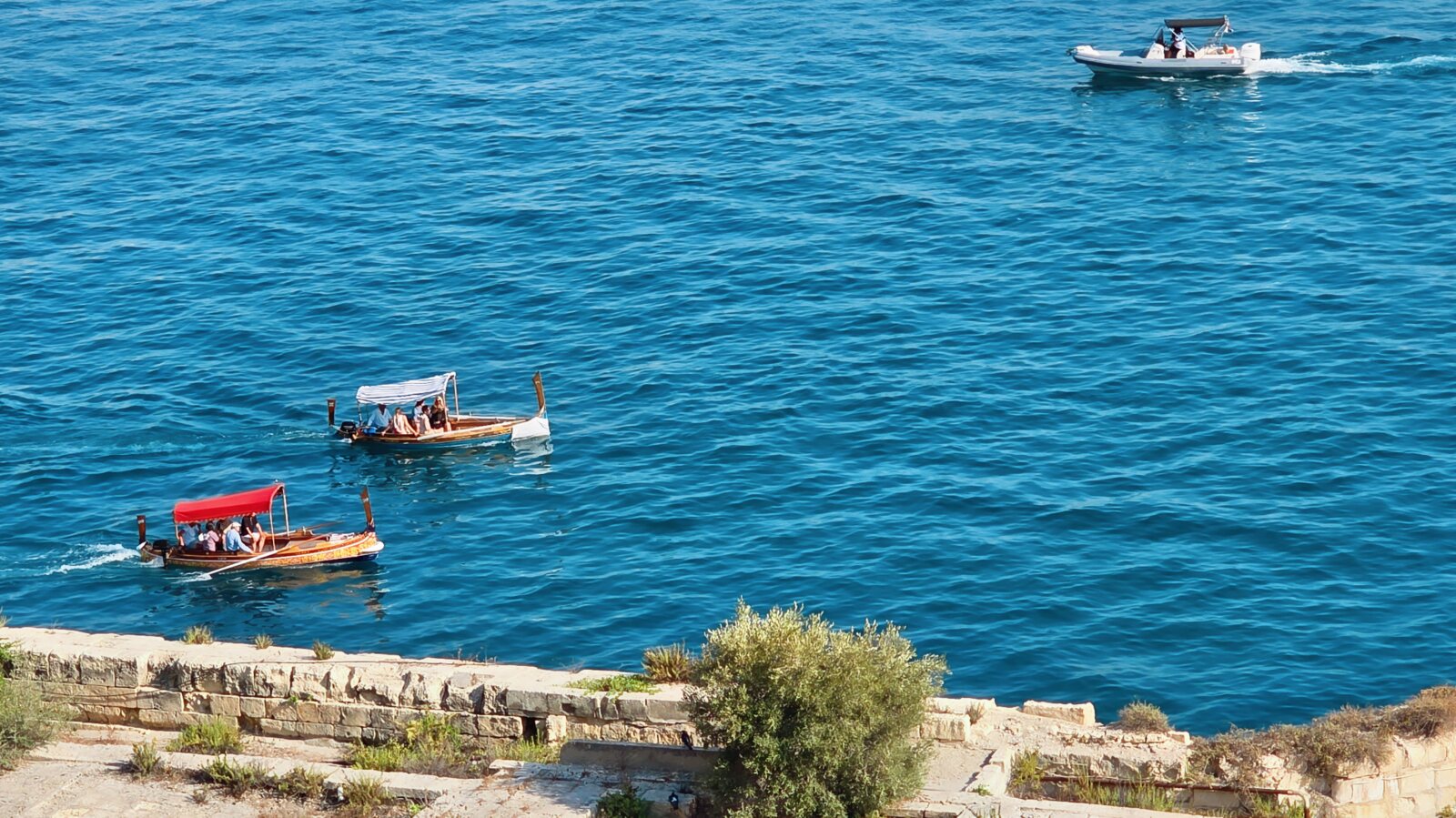 Traditional Maltese dghajsa boats crossing the blue waters of the Grand Harbour